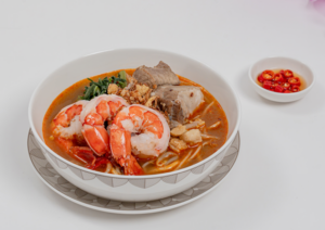 Singapore Style Prawn Noodle Soup (Business Class Main Course) is a Singaporean favourite featuring yellow noodles and vermicelli in a rich, slow-simmered prawn and pork broth. It is served with succulent prawns, tender pork ribs, kang kong, and bean sprouts for a comforting balance of umami and freshness in Singapore Airlines.