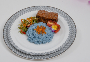 Beef Short Rib Sambal Percik with Nasi Kerabu (Suites and First Class Main Course) draws on the rich culinary heritage of the Nusantara. Tender braised beef short rib is glazed with sambal percik, a coconut-based sauce infused with lemongrass, galangal (blue ginger), and chilli. It is served with nasi kerabu, a herb-infused rice naturally coloured with butterfly pea flower, and a vegetable salad, finished with toasted coconut and lime as served in Singapore Airlines .