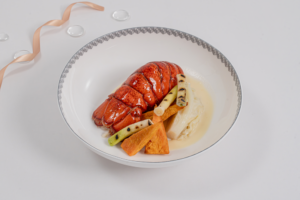 Poached Maine Lobster with Champagne Sauce (Suites and First Class Main Course) features slow-poached Maine lobster shell-on with buttery Savoy cabbage, grilled baby leeks, roasted sweet potatoes, borage cress, and a Champagne cream sauce. 